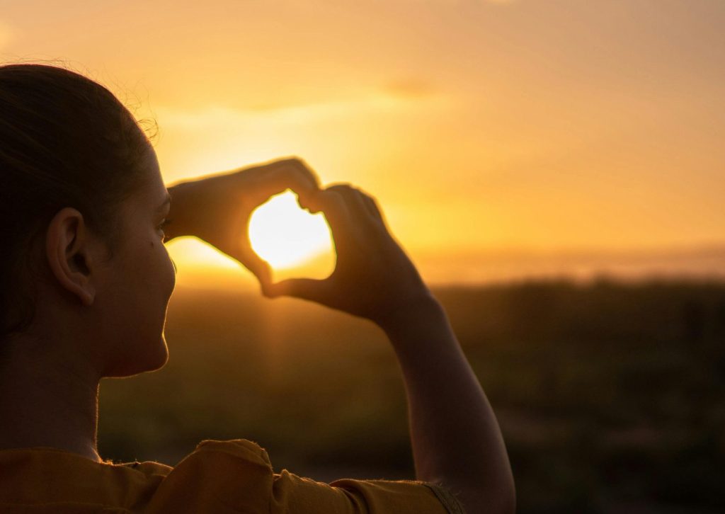 A silhouette of a young woman forming a heart shape at sunset in Kelâat M'Gouna, Morocco.